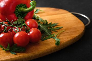 Red ripe fresh cherry tomatoes on branch, pepper and green arugula on wooden cutting board. Healthy food and dieting
