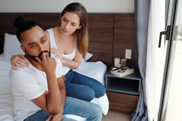 Caring wife reassuring sad offended boyfriend when they are sitting on bed