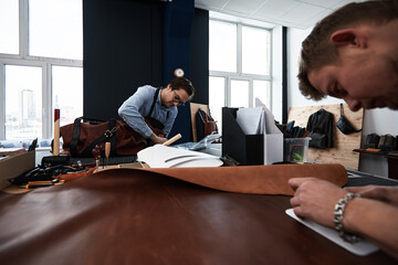 leather craftsmen working making measupenets in patterns at table in workshop studio