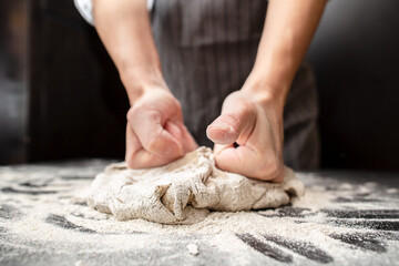 Strong hands of a baker knead dough on a floured table. Bread making.