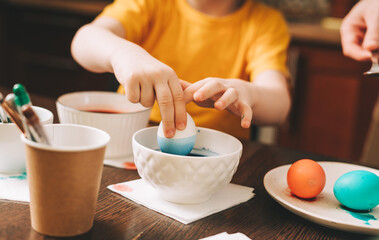Easter day. Cropped close up Kid boy hands painting eggs on wooden background. Child sitting in a kitchen. Preparing for Easter, creative homemade decoration.