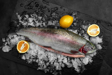 Raw fresh organic dorado or sea bream with lemon on ice cubes over black slate, stone or concrete background.