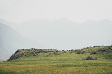 Obraz premium Beautiful foggy mountain landscape with scarecrow on wooden fence around haystack near hills on background of mountains silhouettes in fog. Stack of hay is surrounded by wood fence in vintage tones.
