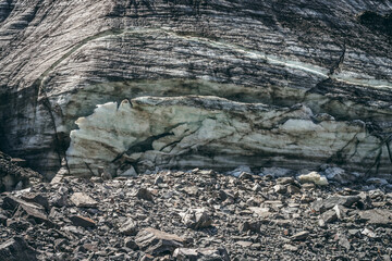 Nature background with icefall near glacier with cracks and scratches. Natural backdrop with icy wall and moraines. Beautiful landscape with shiny glacial wall and stones in sunlight. Glacier texture.