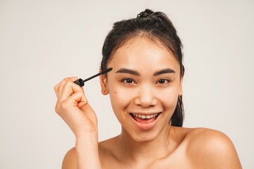 Fototapeta premium Photo of cute woman smiling and using mascara. Isolated over white background. Natural beauty and health
