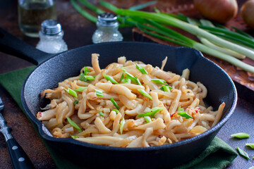 fried calamari in soy sauce with green onions in a cast iron pan, selective focus