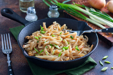 fried calamari in soy sauce with green onions in a cast iron pan, selective focus