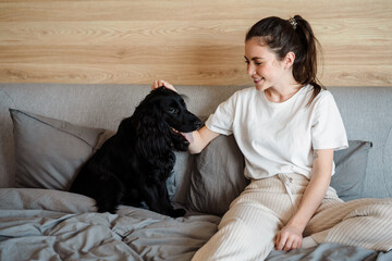 Smiling young brunette woman petting her dog at home