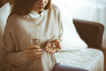 Close-up woman holding pills time to take medications, cure for headache, high blood pressure pain killer drugs at home. Stay at home concept during Coronavirus pandemic