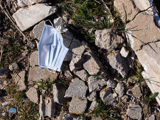 Face mask discarded in field next to garbage