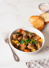 Goulash, beef stew with vegetables and thyme in a white plate with onion and greens.