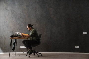 Bearded focused craftsman writing down notes while working with leather