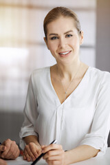 Businesswoman sitting and looking at camera in sunny office