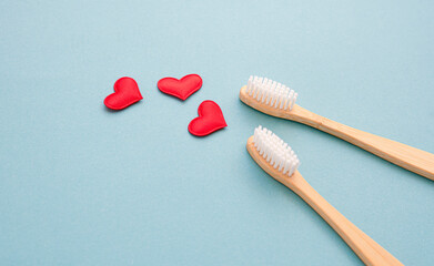 Two bamboo toothbrushes close-up and red hearts on a blue background. Love to brush your teeth. Oral cavity, teeth and gum care. Bleeding gums concept. view from above. copy space for text. Flat lay