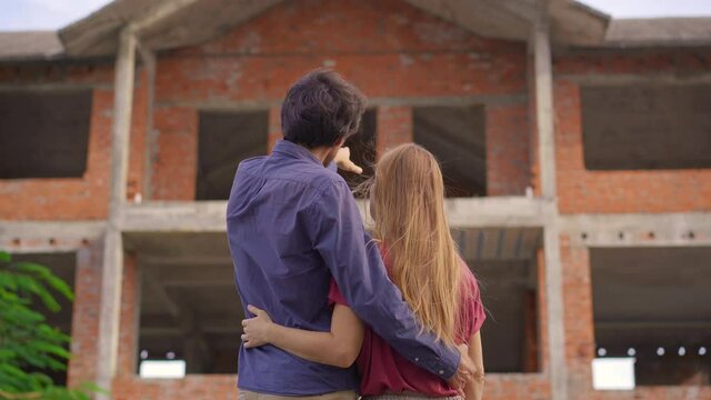 A young couple look at their house that is under construction. They are imagining how they will live happily in this house