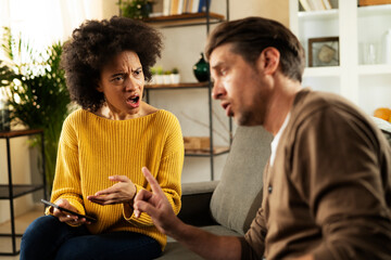 Frustrated young couple arguing at home. Stressed unhappy wife and husband sitting on cauch at home.