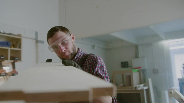 Bearded man in plaid shirt works with wooden blocks in carpenter shop. Checks the equality of the material