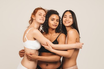 Photo of optimistic young women, multiracial friends wear underwear, hug each other and show their...