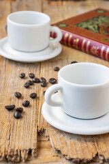 Top view of two empty white coffee cups, on rustic wooden table with coffee beans and book, selective focus, vertical