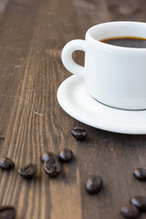 Top view of half white coffee cup with saucer and coffee beans, on dark wooden table, vertical, with copy space