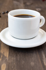 Obraz premium Close-up of white coffee cup with saucer on dark wooden table, vertical, with copy space
