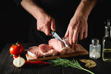 Chef Butcher cutting pork meat with knife on kitchen, cooking food. Vegetables and spices on the kitchen table to prepare delicious lunch