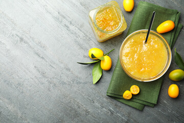 Delicious kumquat jam in bowl and fresh fruits on grey table, flat lay. Space for text