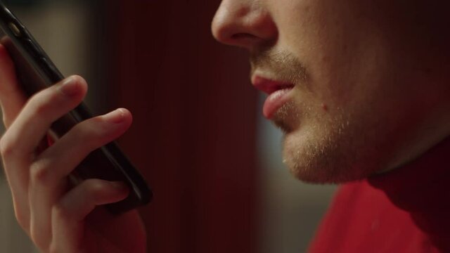 Close-up of cheerful young man using voice input of messages to communicate with friends. Portrait of talking, smiling male student, speaking on phone. 