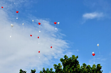 Hoch hinauffliegende rote und weiße Herz-Luftballons mit anhängender Karte vor blauem Himmel