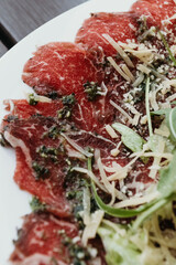 Classic beef carpaccio with cheese and arugula on a ceramic plate, served with lemon. Makro.