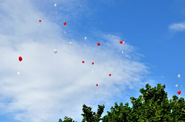 Hoch hinauffliegende rote und weiße Herz-Luftballons mit anhängender Karte vor blauem Himmel