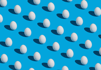 Creative Easter pattern made of white eggs on blue background. Minimal Holiday concept.