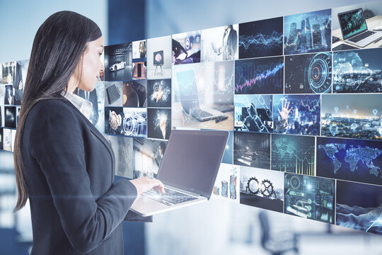 Data flow concept with businesswoman with laptop opposite media wall with video shots.
