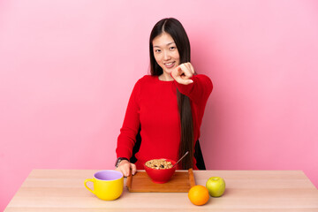 Young Chinese girl  having breakfast in a table pointing front with happy expression