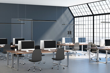 Sunny stylish loft coworking office hall with huge squared window, grey wall, concrete floor and modern furnished workplaces