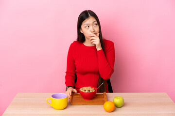 Young Chinese girl  having breakfast in a table having doubts and with confuse face expression