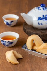 Fototapeta na wymiar Top view of fortune cookies on a plate, teapot and Chinese cups with tea, on wooden table, with selective focus, vertical