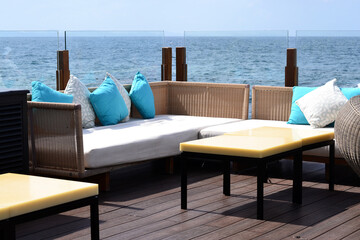 Wicker sofas with soft pillows and low tables in the open air by the sea, and a glass partition