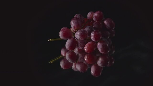 .A bunch of grapes placed on the mirror with a black background are turning.