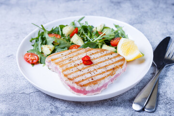 Grilled tuna steak with fresh vegetables, arugula, spinach and lemon. Close-up.