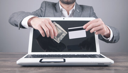 Man holding money and credit card over laptop computer.