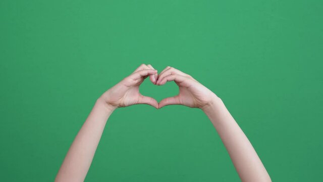 Closeup of kid hands making heart shape gesture on green screen chromakey background. Person forms heart shape using their fingers