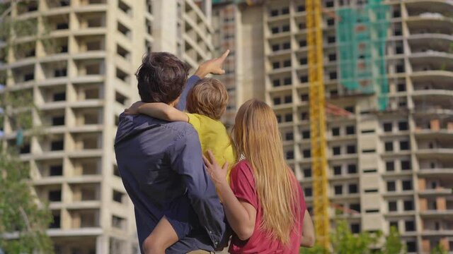 A family father, mother, and son look at a tall building that is under construction. They are discussing where they should buy an apartment