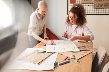 Girls chatting with each other while drawing handmade poster about feminism