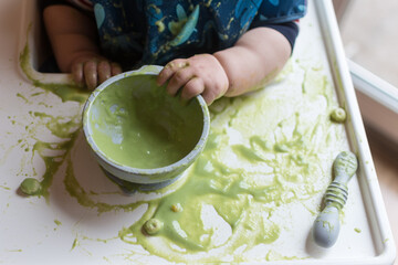 Baby Led Weaning: baby exploring green food puree with hands and making a mess; silicone bowl and spoon