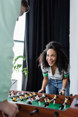 laughing african american businesswoman playing table football with colleague on blurred foreground