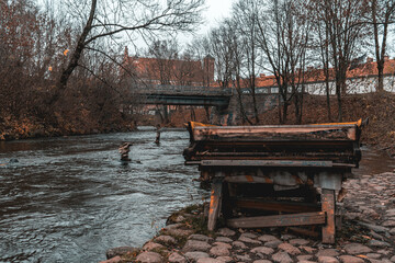 Old and abandoned wooden piano by the coast of the Vilnia river near Uzupis with the Bernardinu Bridge in the background in Vilnius, Lithuania