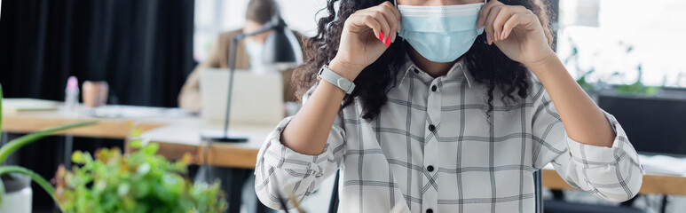 partial view of african american businesswoman adjusting medical mask in office, banner