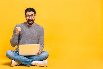 Successful winner! Portrait of a happy young bearded man using laptop and celebrating success or...