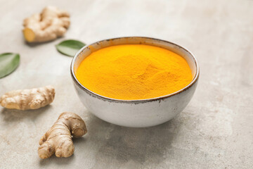Bowl with turmeric powder and roots on grunge background